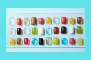 Row of colorful gummy candies arranged on a white tray with a turquoise background.