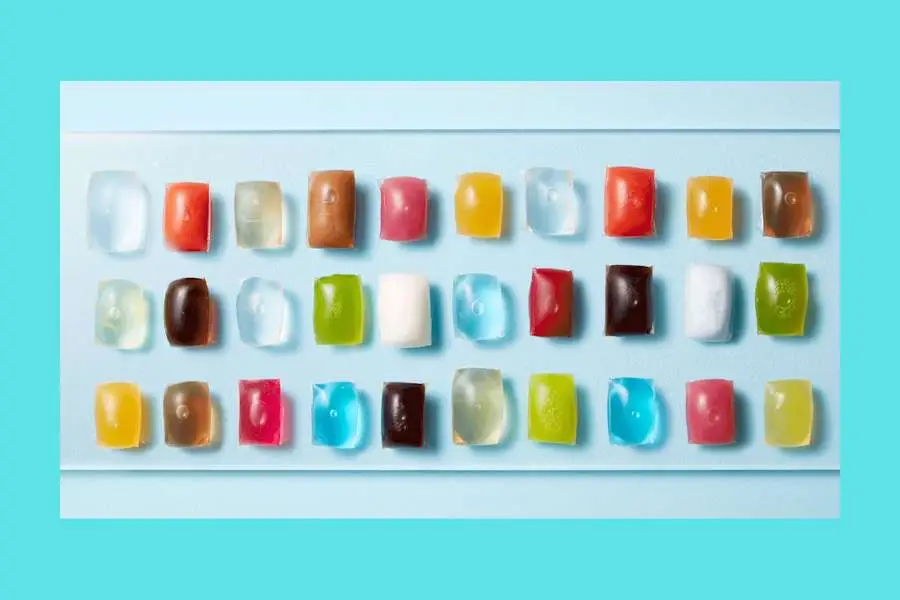 Row of colorful gummy candies arranged on a white tray with a turquoise background.